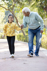 Senior man holding stick while walking with granddaughter at park