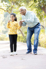 Senior man holding stick while walking with granddaughter at park