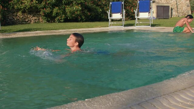 A preteen boy jumps into an outdoor pool, swims. Water play allows children to explore environment. Child gain confidence in and control of his body. IT, Borgagne, 6.10.2021 