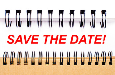 Text SAVE THE DATE on white paper between white and brown spiral notepads.