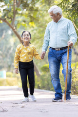 Senior man holding stick while walking with granddaughter at park