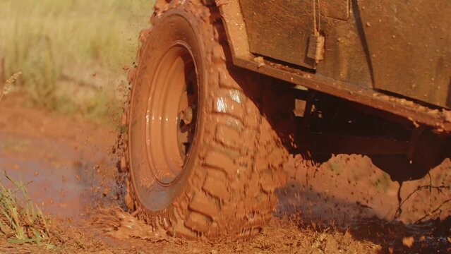 Utility vehicle driving mud pit obstacle spreading splashes to sides on race on off road, closeup. SUV drives through dirty road