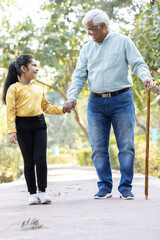 Obraz premium Senior man holding stick while walking with granddaughter at park