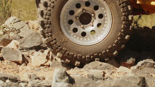 Dusty SUV is driving on cobblestones in off road, side view. Car carefully drivings rocky section of road in race