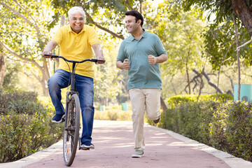Cheerful senior man riding bicycle while son running at park