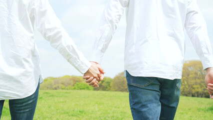 手を繋いで草原を歩くカップル