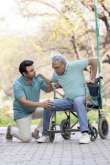 Fototapeta na wymiar Young man assisting a senior man in a wheelchair at park