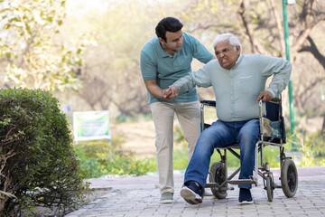 Young man assisting a senior man in a wheelchair at park