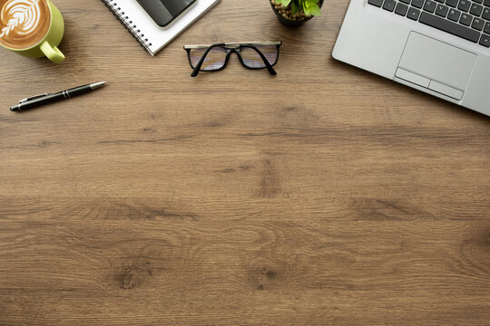Blank notebook is on top of wood office desk table with laptop computer cup of latte coffee and office supplies. Top view with copy space, flat lay.