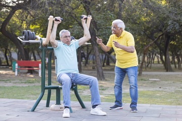 Two senior man having fun while exercising in open air gym at park