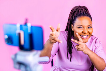 dark skinned woman laughing and shooting social media stories in pink wall background
