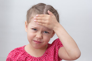 Child with headache holding hand on forehead on white background caucasian little girl 5-6 years in red looking at camera - obrazy, fototapety, plakaty