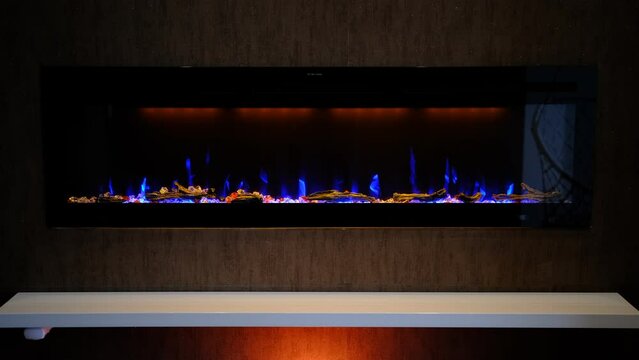 view on electric fireplace with artificial sparkling flame, decor for the interior, blue flame on crystals with orange backlighting.