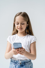 Fototapeta premium smiling girl in earphones using mobile phone isolated on grey.