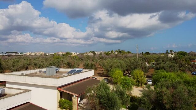 Apartments for rent with parking next to the olive grove. Choosing a place for a summer vacation away from the city. The drone camera pans up from the garden lawn. IT, Borgagne, 6.10.2021 