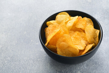 Potato chips. Fast food. Crispy potato chips ceramic black bowl with sour cream sauce and onions in wooden stand on gray kitchen table concrete background. American tradition. Hot BBQ. Top view.