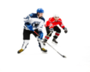 Fototapeta na wymiar Rival hockey players fight for control of the puck - out of focus hockey player on ice - blur hockey match on background