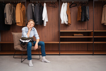 The European blond boy teenager brings wardrobe order, puts everything in its place, hides things in boxes. Wardrobe with women's, men's and child's clothing. Closet.