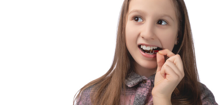 A cute little girl is putting on an orthodontic appliance. The concept of oral hygiene in childhood. Studio photo on a white background.