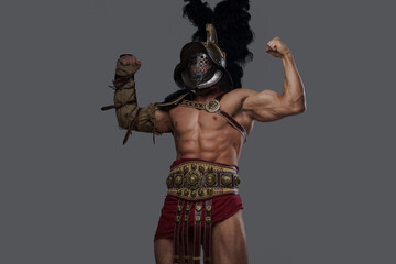 Shot of handsome greek warrior with nude muscular body showing his strength against grey background.