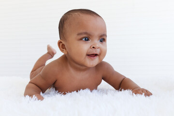 Portrait of a six month crawling African American baby on fluffy white rug, happy smiling adorable sweet little girl kid lying on bed in bedroom, childhood and baby care concept