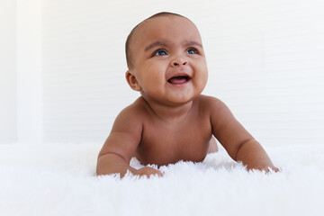 Portrait of a six month crawling African American baby on fluffy white rug, happy smiling adorable sweet little girl kid lying on bed in bedroom, childhood and baby care concept