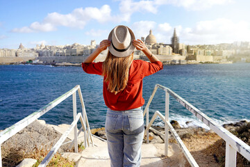 Holidays in Malta. Back view of beautiful girl enjoying view of Valletta cityscape with the blue water of Mediterranean sea. - obrazy, fototapety, plakaty