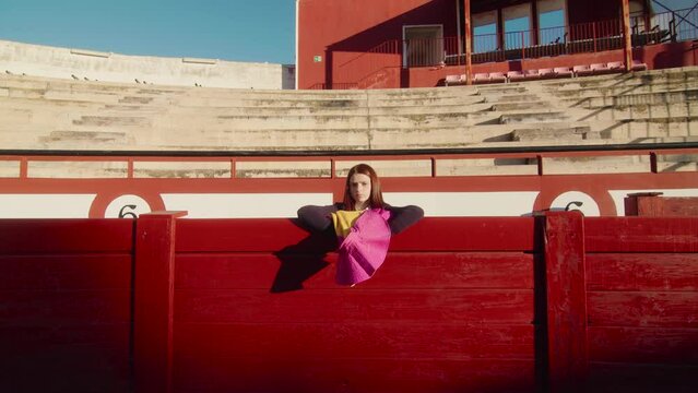 Young Female Bullfighter With Muleta Standing Behind Red Wooden Fence Of Bullring. - static