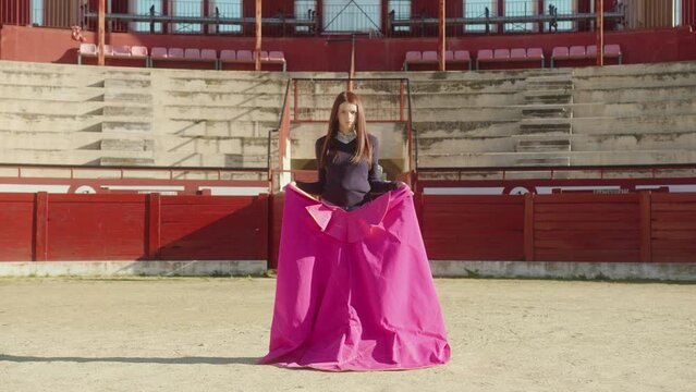 Young Female Bullfighter With Muleta Standing In Middle Of Bullring With Empty Tiered Rows In The Background. - static