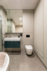Modern bright bathroom with beige wall. Washbasin with turquoise cupboard and mirror. Wall with molding.