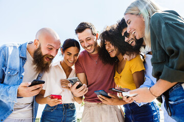 Young group of happy people smiling while using mobile phone together - Smiling multiracial friends...