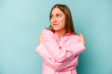 Fototapeta premium Young caucasian woman isolated on blue background hugs, smiling carefree and happy.