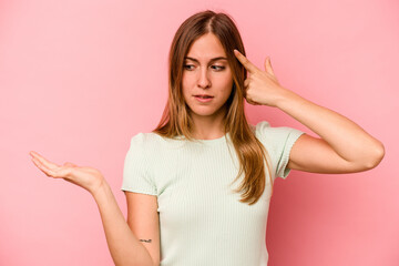 Fototapeta premium Young caucasian woman isolated on pink background holding and showing a product on hand.