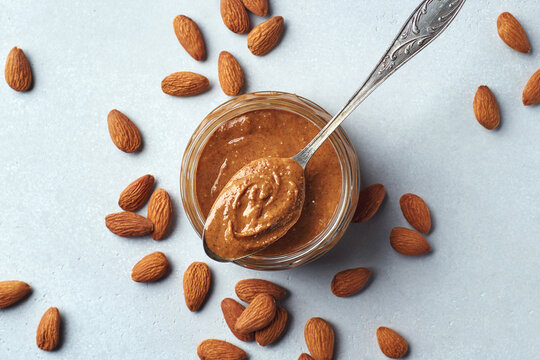 Glass jar and spoon of almond butter on light gray background