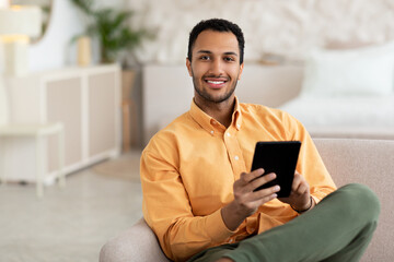 Smiling young Arab man using digital tablet at home