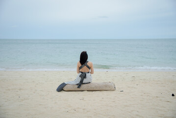 Rearview of a lonely woman sitting on the log and looking to the sea.