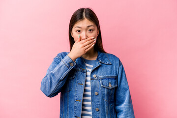 Young Chinese woman isolated on pink background covering mouth with hands looking worried.