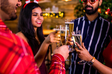 group of four indian friends cheering with champagne flutes and looking happy while having party on the kitchen at stay home quarantine corona virus outbreak party