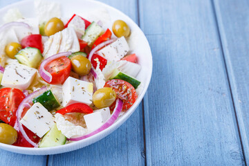 Greek salad. Traditional Greek dish. Healthy vegetarian food. Fresh vegetables and feta cheese in a white plate. Close-up, blue background.