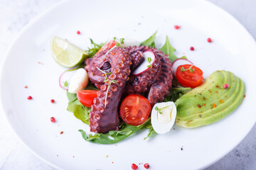 Warm salad with octopus, cherry tomatoes, avocado, arugula, quail eggs, radish and lime on a white...