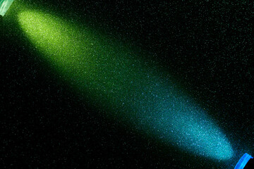 Gradient beam of light from light green and blue colors on a black grainy background