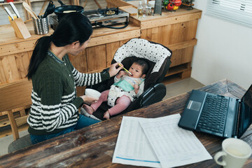 korean female freelancer taking time from work is giving solid food to baby in her study. asian...