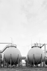 Spherical gas storage tank of chemical industry petrochemical plant under grey sky black and white BW vertical with copyspace.