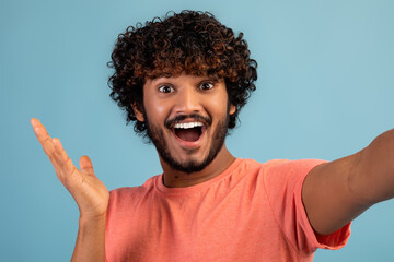 Emotional hindu guy taking selfie on blue studio background