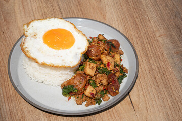 Closed up Famous Thai food padkaprow.  A plate of delicious Stir fried  fresh holy basil mix pork minced and sausage with toped rice fried egg on wooden background.