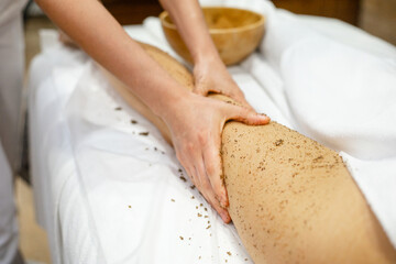 Body scrub in spa salon. Coffee scrub. Masseur kneads and scrubs the heels of a young woman