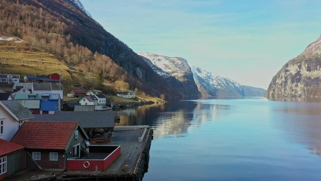 Beautiful early morning in Undredal village close by the majestic Aurlandsfjord in Norway - Low altitude sunrise aerial close to sea passing boathouse