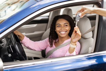 Happy black woman sitting in new car taking keys