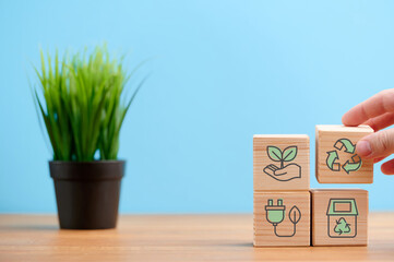 Circular economy concept, recycle, environment, reuse, manufacturing, waste, consumer, resource. Sustainable development. Hand put wooden cubes; the symbols of circular economy on blue background