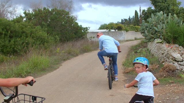 8.10.2021 Borgagne, Puglia, Italy. The family rides bicycles on the road in the village, the cyclist is ahead of them.